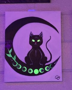 Black cat on a crescent moon with blacklight reactive paint at Arte Bella on 4th